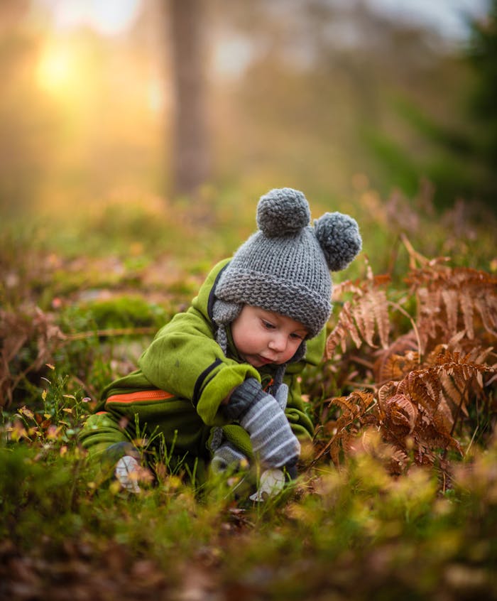 about-us-02 A cute baby in a knit hat and green outfit exploring nature during sunset.